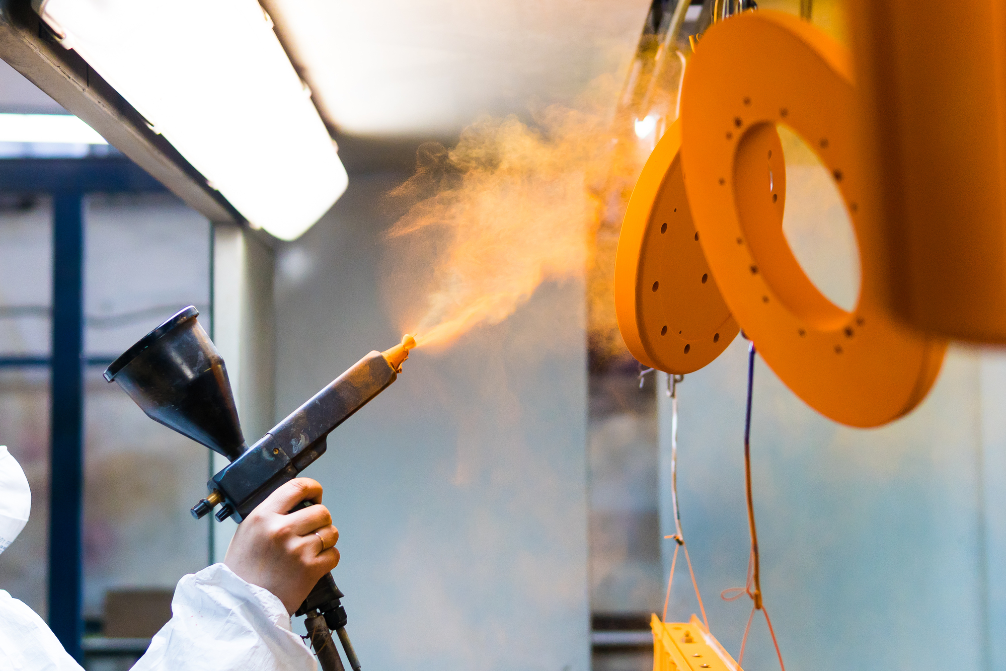 A man in a protective suit sprays powder paint on metal products.